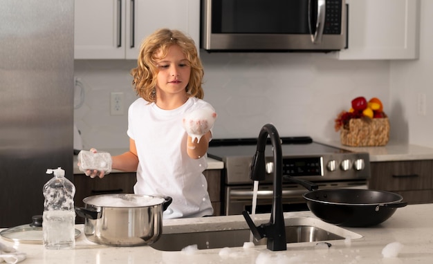 Child boy washing dishes in the kitchen interior dishwashing liquid with a sponge on kitchen sink ch