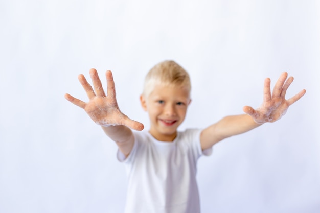 Child boy in a white t-shirt shows hands in foam