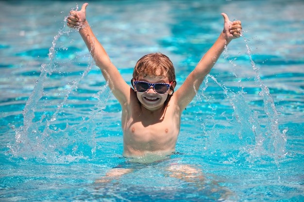 Child boy with thumbs up raised hands swim in swimming pool splashing in water having fun leisure ac