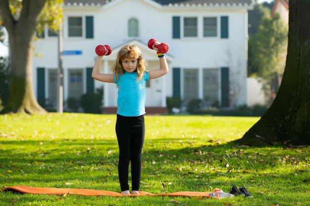 Child boy working out with dumbbells on park background kids sport outdoor