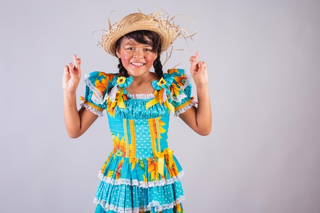 Child Brazilian girl with Festa Junina clothes fingers crossed lucky sign cheering