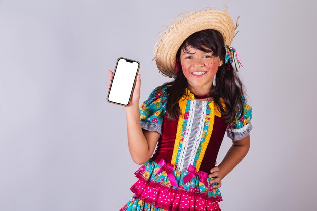 Child Brazilian girl with festa junina clothes showing smartphone screen