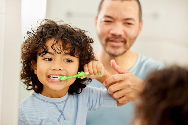 Foto il bambino si lava i denti e il padre impara in un bagno con la salute dentale e la pulizia lo spazzolino da denti di routine mattutino e il bambino con il papà insieme mostrano le cure igieniche allo specchio a casa con la toelettatura