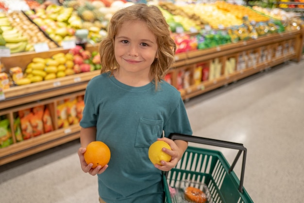 スーパーマーケットで果物を買う子供 レモンとオレンジを持った子供 小さな男の子が新鮮な野菜を買う