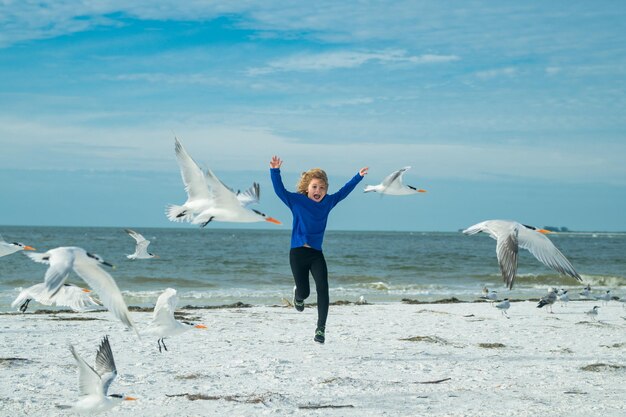 Child chasing birds near summer beach excited boy running on the beach with flying seagulls birds