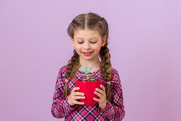 A child in a checkered purple dress holds a green plant in a red pot.