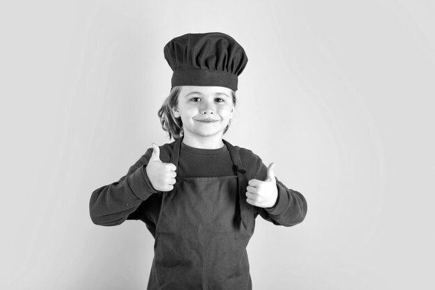 Child chef cook prepares food on isolated studio background Kids cooking Teen boy with apron and chef hat preparing a healthy meal