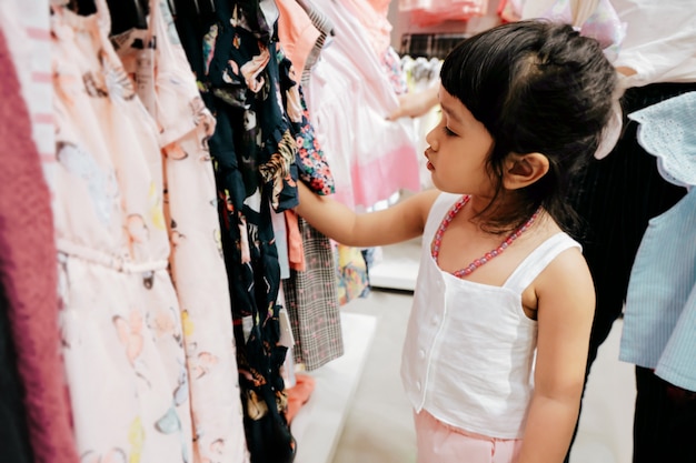 Foto bambino che sceglie i suoi abiti dal portabiti per bambini nel negozio di abbigliamento.