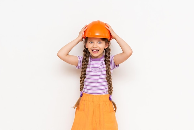 建設用ヘルメットをかぶった子供が両手で頭を抱えている美しい少女が白い孤立した背景で修理の準備をしています