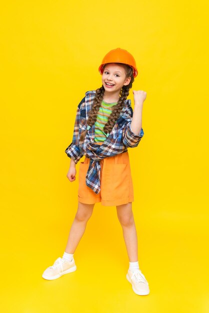 A child in a construction helmet A little teenage girl rejoices at the upcoming renovation in the children's room The profession of an engineer for a child Yellow isolated background