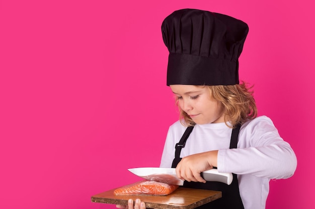 Child cook hold cutting board with fish salmon steak and knife Child chef cook studio portrait Kids cooking Teen boy with apron and chef hat