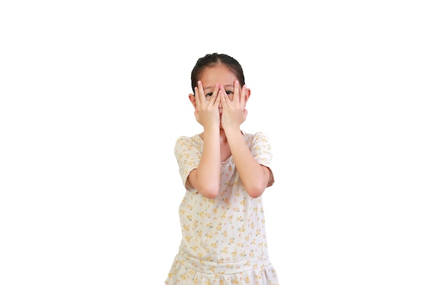 Child covering eyes while watching through gap in fingers on white