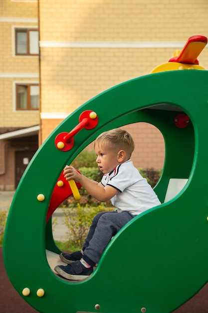 Photo child, cute caucasian boy riding swing on playground near his house in a town