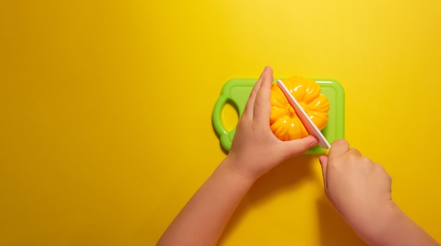 Foto un bambino taglia un peperone giocattolo su uno sfondo giallo con un coltello giocattolo