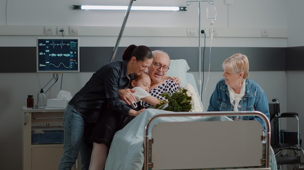 Child and daughter of sick patient coming to visit in hospital ward. Retired man with disease enjoying family of woman and little girl visiting with flowers at medical clinic. Visitors