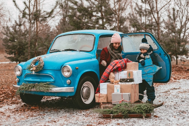 Child decorated with a blue retro car with festive christmas tree branches gift boxes in craft wrapp...