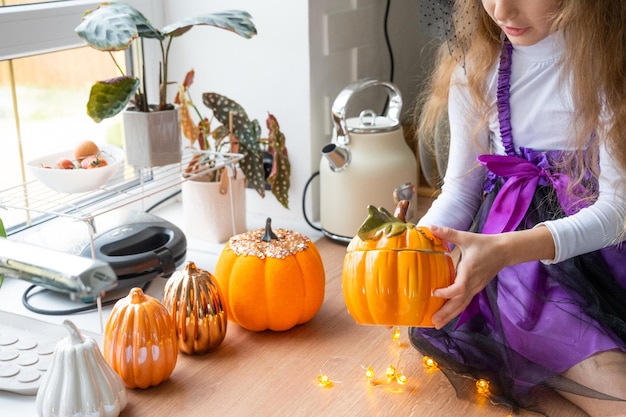 Child decorates the kitchen in home for Halloween Girl in a witch costume plays with the decor for the holiday bats jack lantern pumpkins Autumn comfort in house Scandistyle kitchen loft