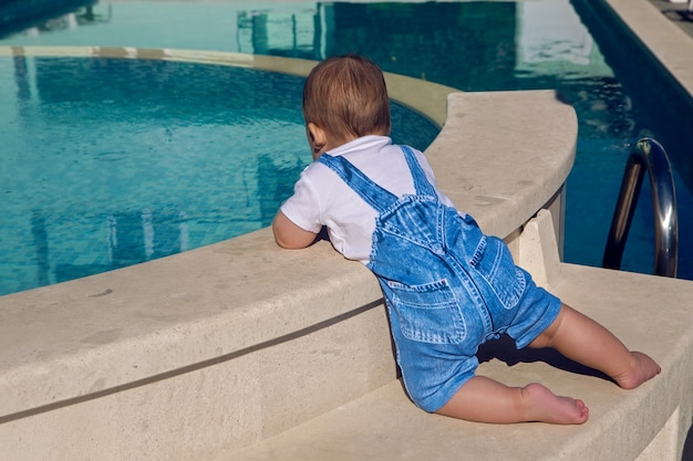 Il bambino in un vestito di jeans si siede sul bordo della piscina
