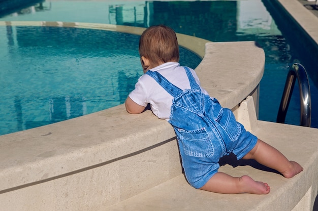 デニムのスーツを着た子供がプールの端に座っています