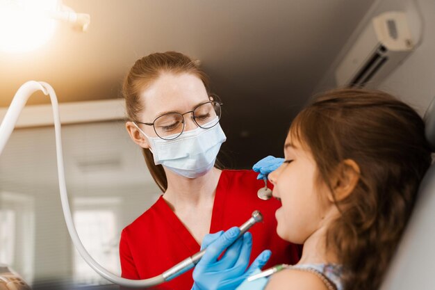 Child dentist with dental drill treats child girl in dentistry clinic Dental filling for child patient