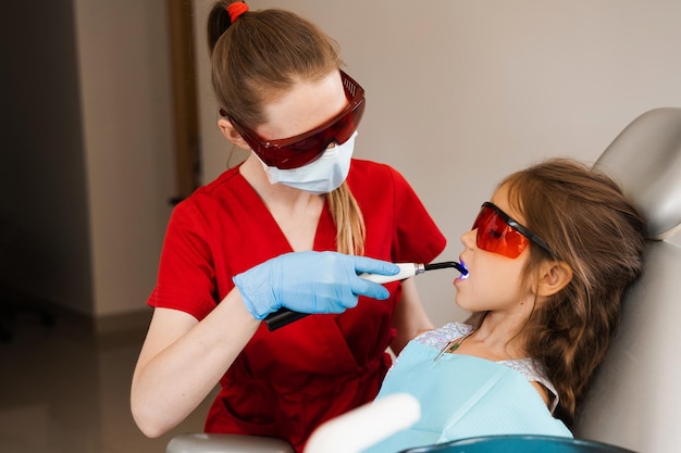 Child dentistry Uv illumination of photopolymer tooth filling procedure Child dentist in red protective glasses treats and removes caries in a patient