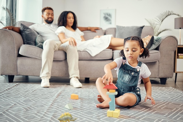 Photo child development and toy blocks while learning motor skill and colors while building a tower in lounge at home with parents or adult supervision girl kid playing and fun with educational activity