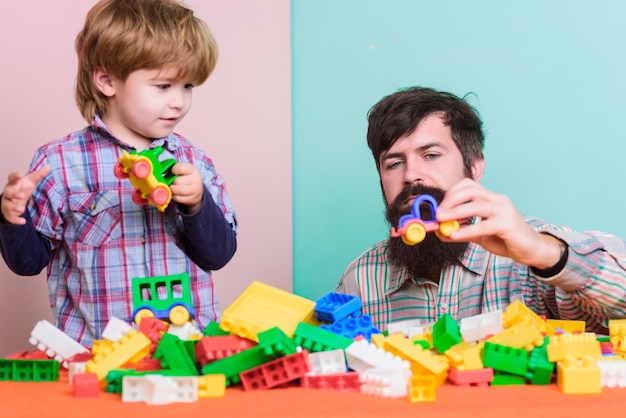 Child development and upbringing. Father and son have fun. Bearded hipster and boy play together. Dad and child build plastic blocks. Importance of playing together. Child care concept. Happy family.