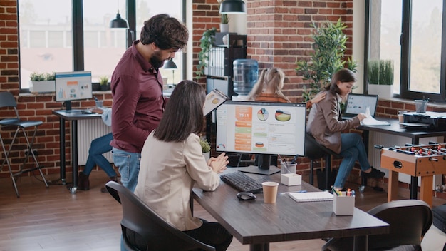 Child distracting multi ethnic colleagues in the office while her mother is talking with colleague about company growth, charts and startup. Working mother talking to man about project strategy and pl