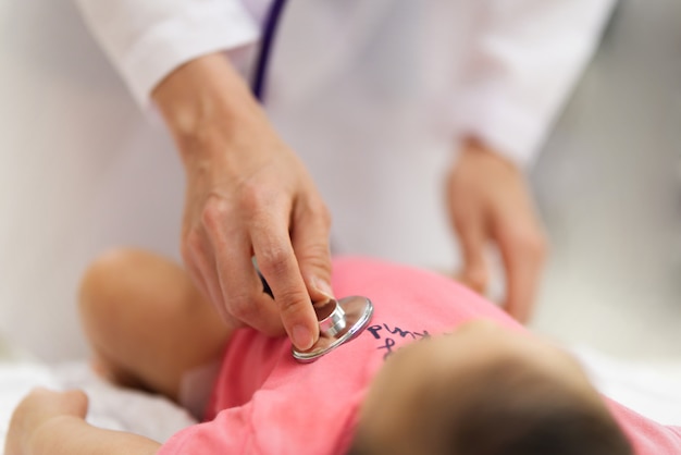 Foto il medico del bambino sta ascoltando la frequenza cardiaca del polso del neonato sveglio che si trova sul letto usando lo stetoscopio.