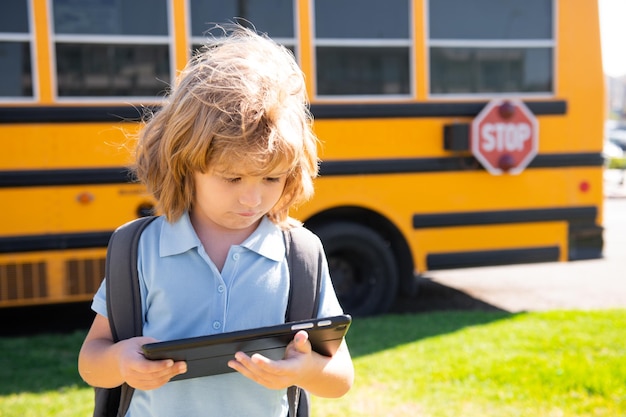 Child does school homework with tablet in the park near school bus school kid outdoor