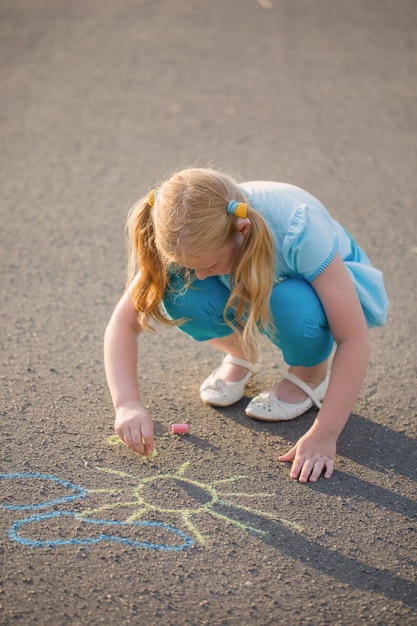 The child drawing a chalk on asphalt