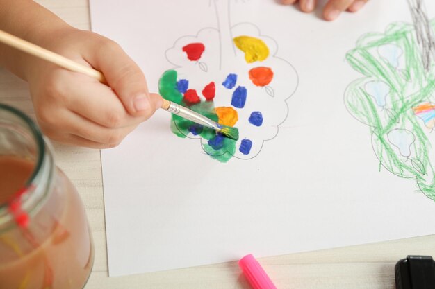 Photo child drawing tree with bright paints on paper closeup