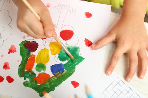 Child drawing with bright paints on paper closeup