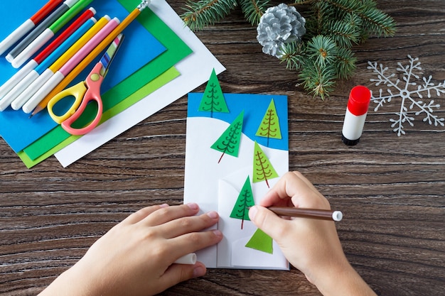 The child draws the details of the manufacture of paper cards Christmas Crafts for a child