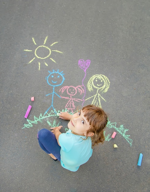 Child draws a family on the pavement with chalk. Selective focus.