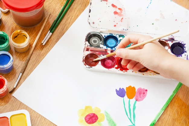 A child draws flowers by paint