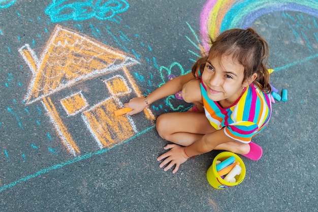 The child draws a house and a rainbow on the asphalt with chalk