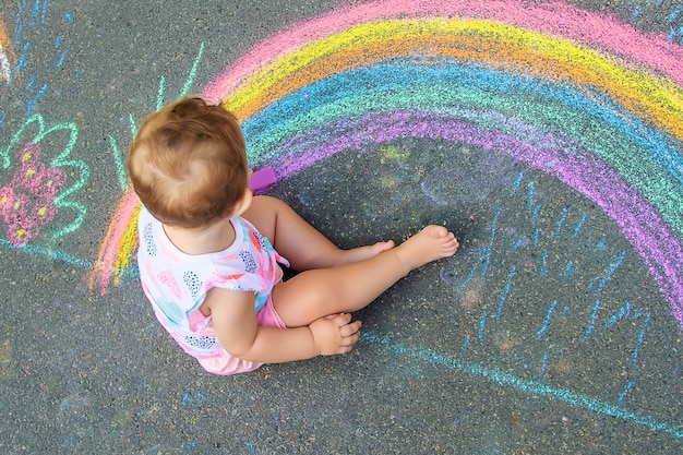 The child draws a house and a rainbow on the asphalt with chalk