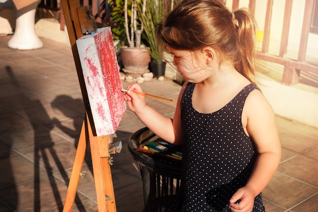 The child draws on a malbert. A girl runs a brush across the canvas with paint