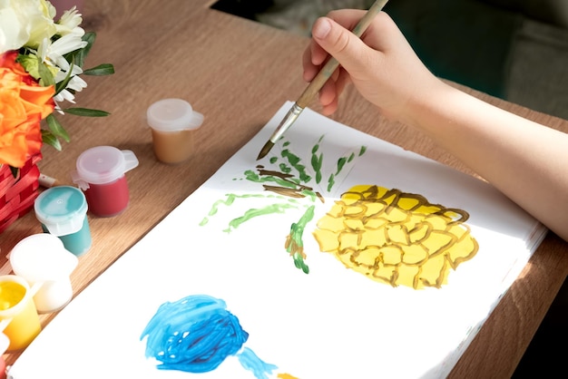 Child draws pineapple fruit with paints in album close up