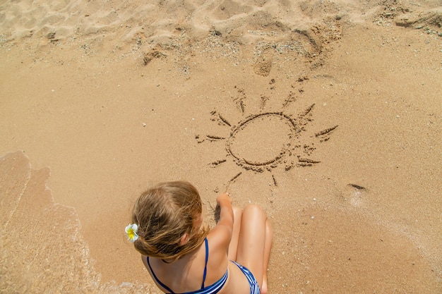 Child draws in the sand on the beach