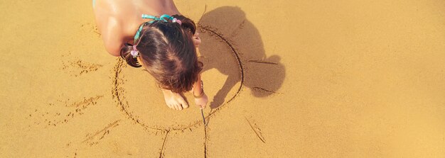 A child draws a sun on the beach