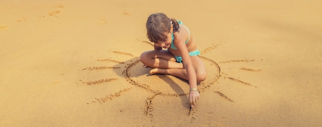 A child draws a sun on the beach