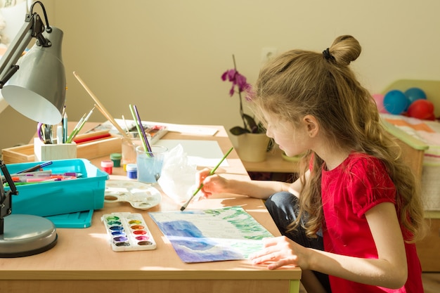 Child draws watercolor at the table at home