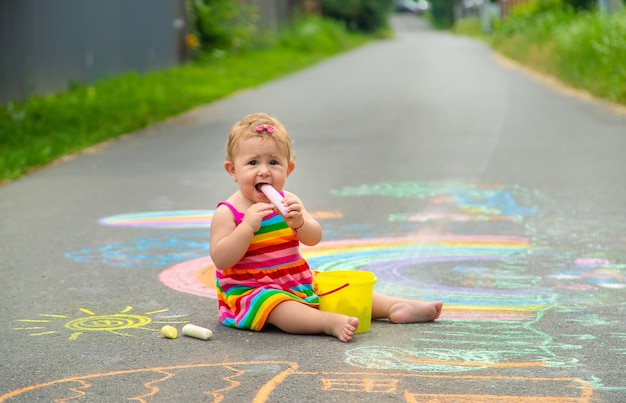 The child draws with chalk on the asphalt. Selective focus. Kid.