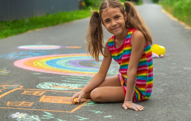 The child draws with chalk on the asphalt. Selective focus.