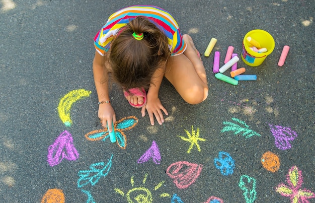 The child draws with chalk on the asphalt