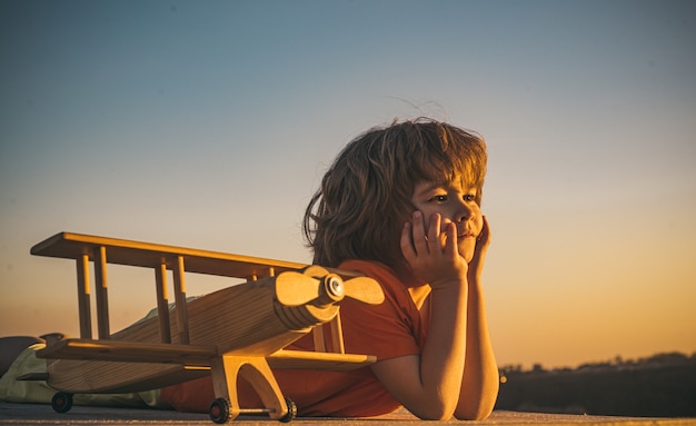 Child dreams and imagination concept dreaming child playing with toy wooden airplane against summer ...