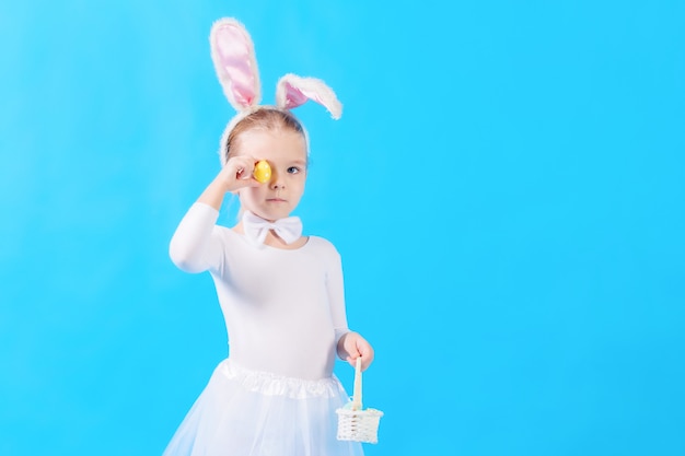 Un bambino vestito da coniglietto pasquale bianco. la bambina tra le mani tiene un cestino e un uovo di pasqua. copia spazio.