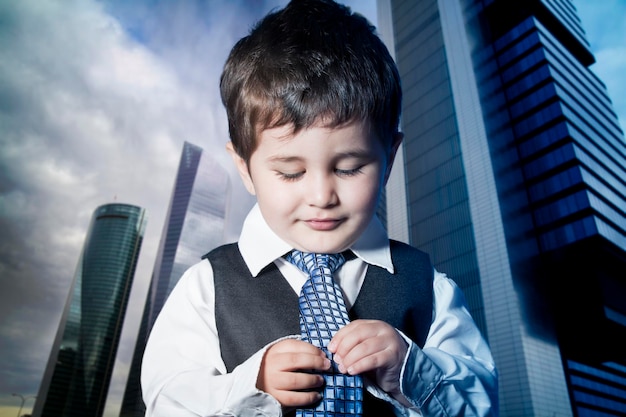 Child dressed businessman with hands in his tie and skyscrapers in the background